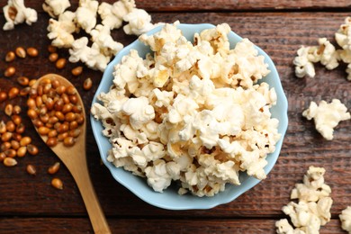 Photo of Tasty popcorn and corn kernels on wooden table, flat lay