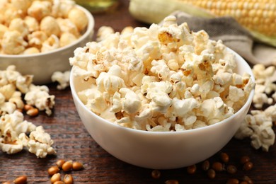 Photo of Tasty popcorn and corn kernels on wooden table, closeup