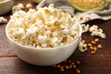 Photo of Tasty popcorn and corn kernels on wooden table, closeup