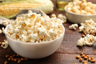 Photo of Tasty popcorn, corncob and corn kernels on wooden table, closeup
