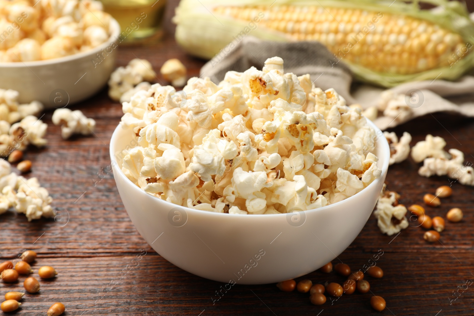 Photo of Tasty popcorn, corncob and corn kernels on wooden table, closeup