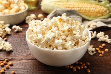 Photo of Tasty popcorn, corncob and corn kernels on wooden table, closeup