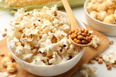 Photo of Tasty popcorn and corn kernels on white table, closeup
