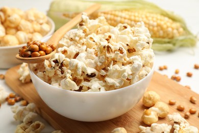 Photo of Tasty popcorn and corn kernels on white table, closeup