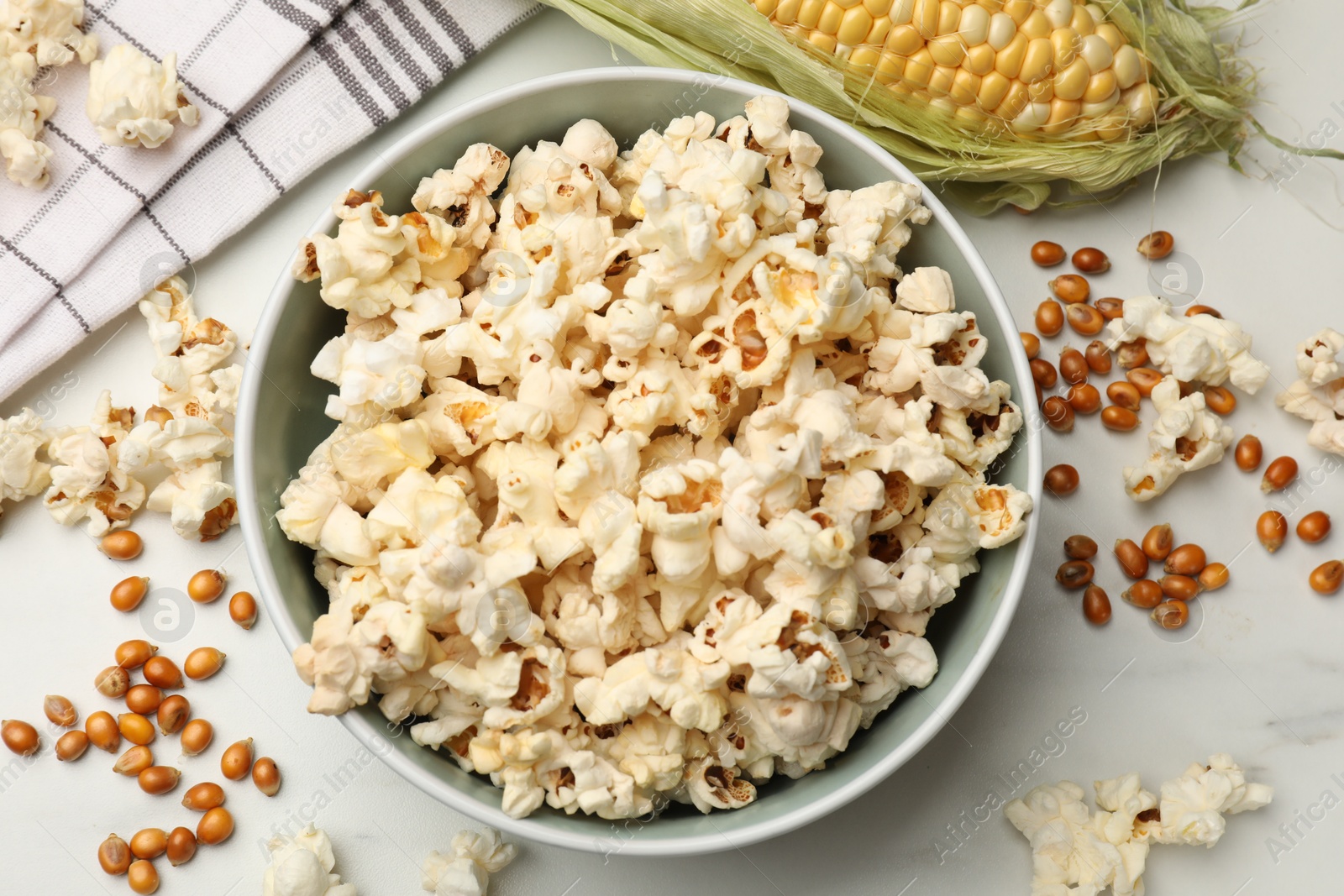 Photo of Tasty popcorn, corncob and corn kernels on white marble table, flat lay