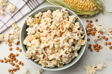 Photo of Tasty popcorn, corncob and corn kernels on white marble table, flat lay