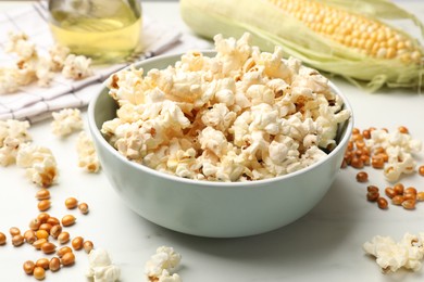 Photo of Tasty popcorn and corn kernels on white marble table, closeup