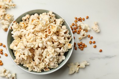 Photo of Tasty popcorn and corn kernels on white marble table, flat lay
