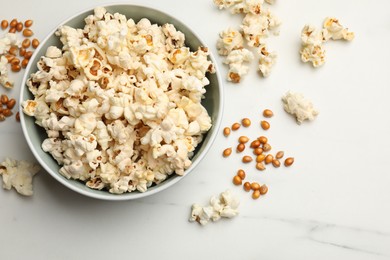 Photo of Tasty popcorn and corn kernels on white marble table, flat lay