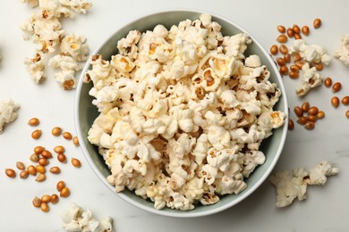 Photo of Tasty popcorn and corn kernels on white marble table, flat lay