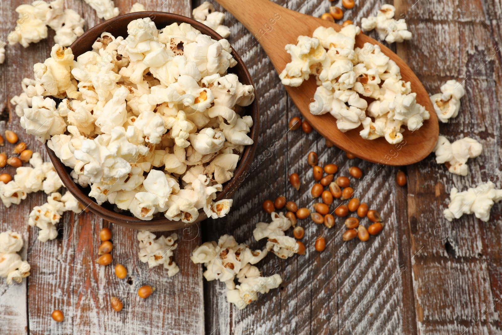 Photo of Tasty popcorn and corn kernels on wooden table, flat lay