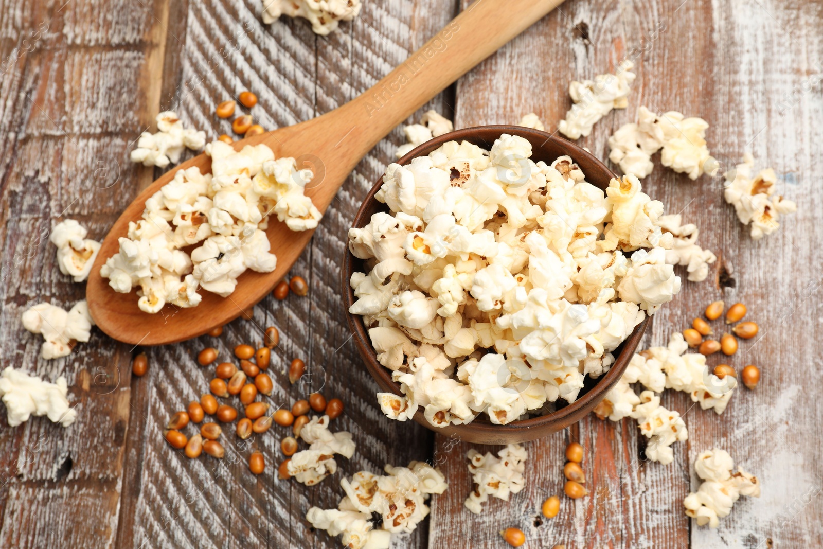 Photo of Tasty popcorn and corn kernels on wooden table, flat lay