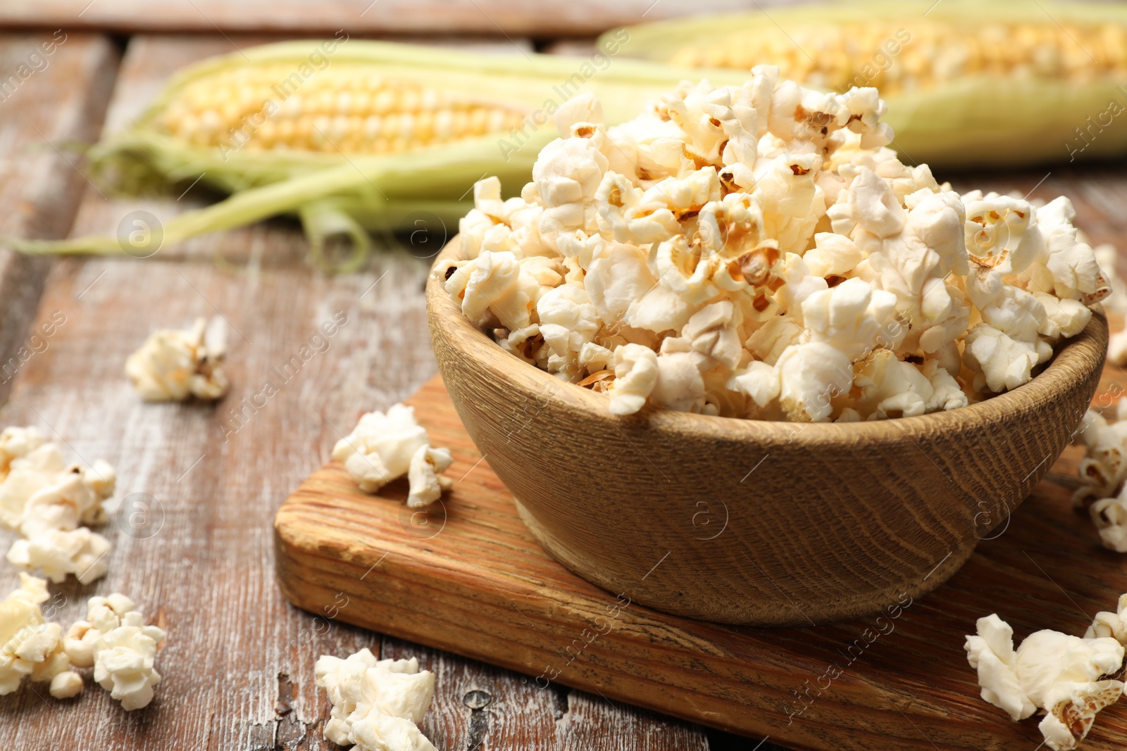 Photo of Tasty popcorn and corncobs on wooden table, closeup. Space for text