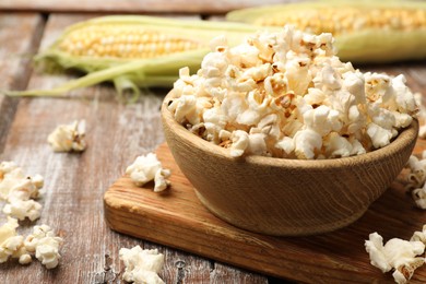 Photo of Tasty popcorn and corncobs on wooden table, closeup. Space for text