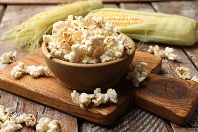 Photo of Tasty popcorn and corncobs on wooden table, closeup