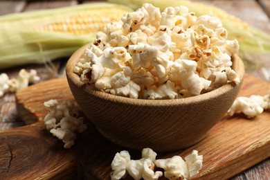 Photo of Tasty popcorn and corncobs on wooden table, closeup