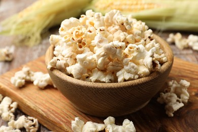 Photo of Tasty popcorn and corncobs on wooden table, closeup