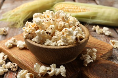 Photo of Tasty popcorn and corncobs on wooden table, closeup