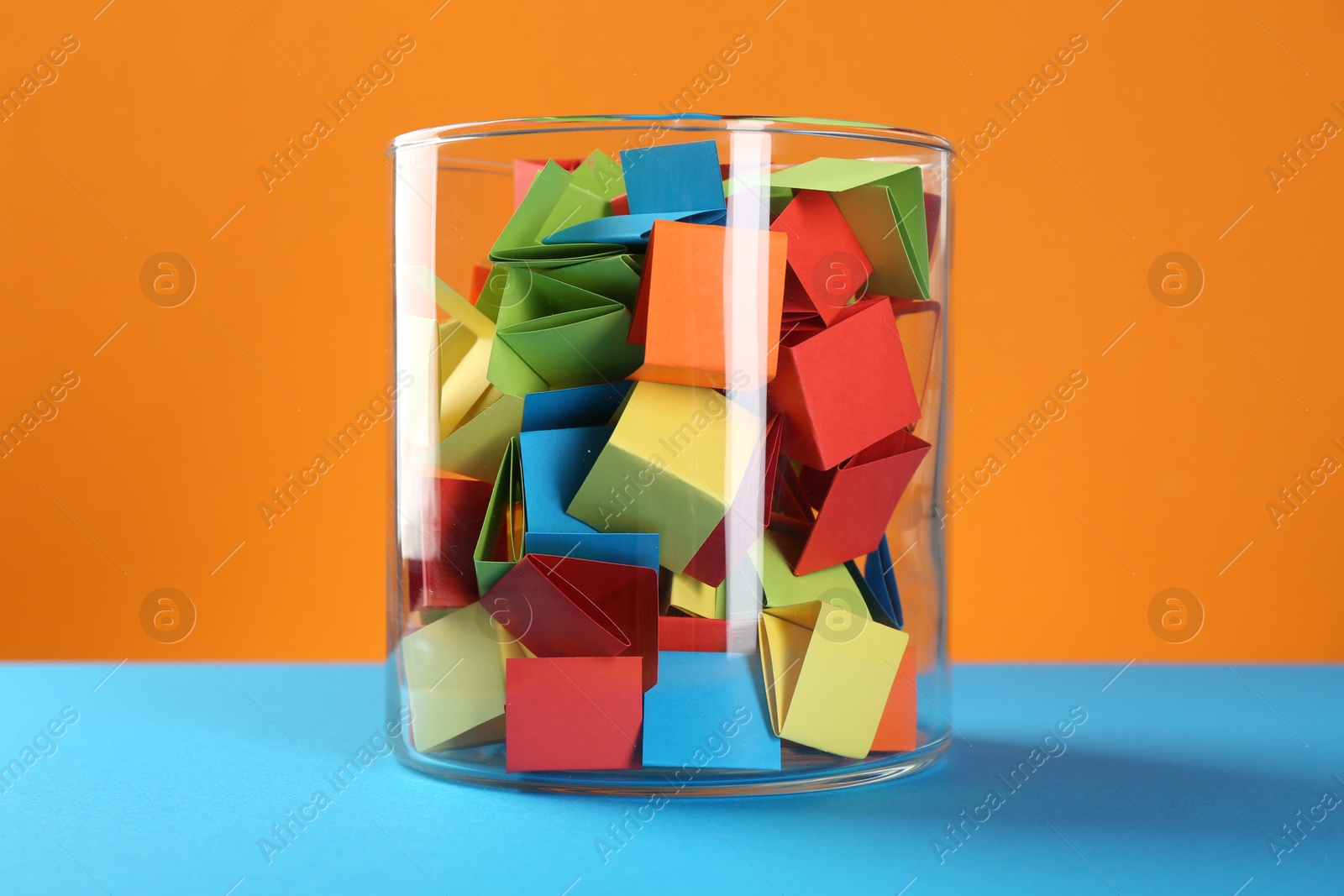 Bright paper pieces in glass jar on color background Photo of Bright paper pieces in glass jar on color background