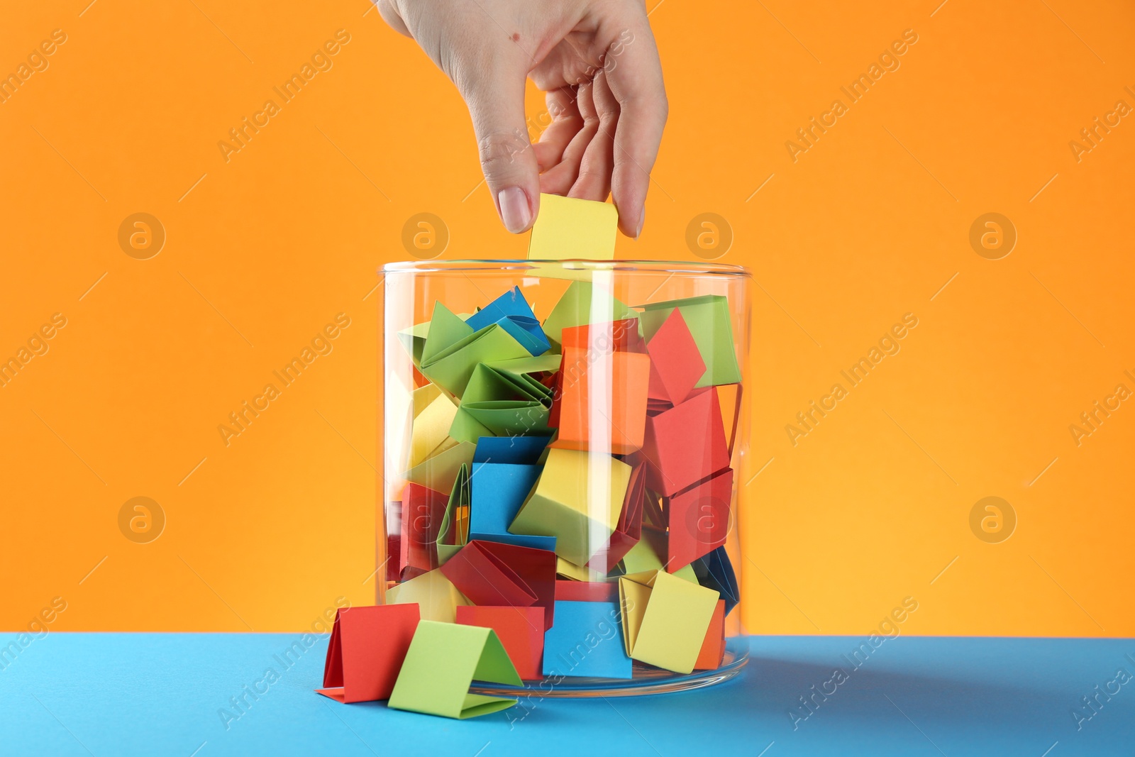 Woman taking yellow paper piece from glass jar on color background, closeup Photo of Woman taking yellow paper piece from glass jar on color background, closeup