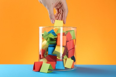 Photo of Woman taking yellow paper piece from glass jar on color background, closeup