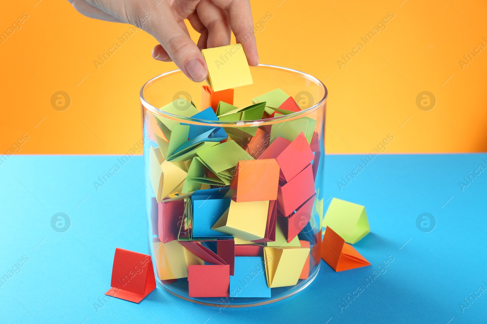 Woman taking yellow paper piece from glass jar on color background, closeup Photo of Woman taking yellow paper piece from glass jar on color background, closeup