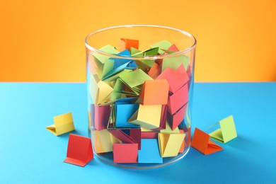 Photo of Bright paper pieces in glass jar on color background, closeup