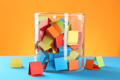 Photo of Bright paper pieces in glass jar on color background, closeup
