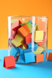 Photo of Bright paper pieces in glass jar on color background, closeup