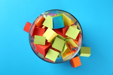Photo of Colorful paper pieces in glass jar on light blue background, top view