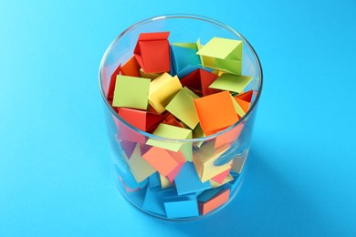 Photo of Colorful paper pieces in glass jar on light blue background, closeup