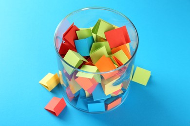 Photo of Colorful paper pieces in glass jar on light blue background, closeup