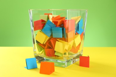 Photo of Bright paper pieces in glass jar on color background, closeup