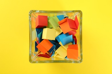 Photo of Colorful paper pieces in glass jar on yellow background, top view