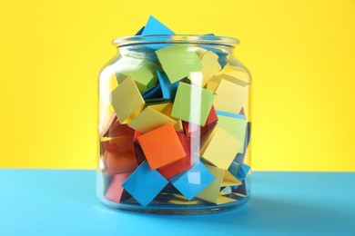 Photo of Bright paper pieces in glass jar on color background, closeup