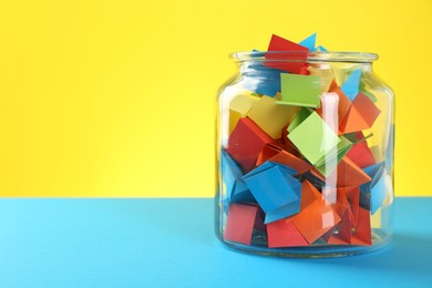Photo of Bright paper pieces in glass jar on color background, closeup. Space for text