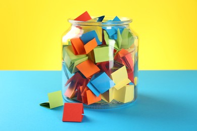 Photo of Bright paper pieces in glass jar on color background, closeup