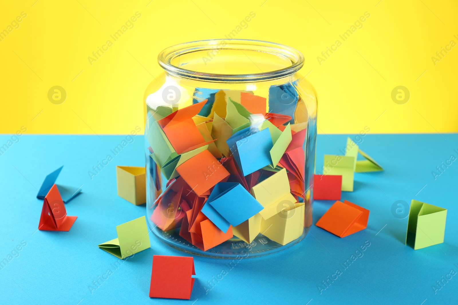 Bright paper pieces in glass jar on color background, closeup Photo of Bright paper pieces in glass jar on color background, closeup