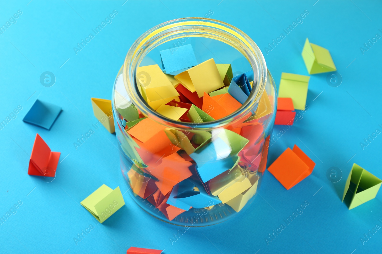 Colorful paper pieces in glass jar on light blue background, closeup Photo of Colorful paper pieces in glass jar on light blue background, closeup
