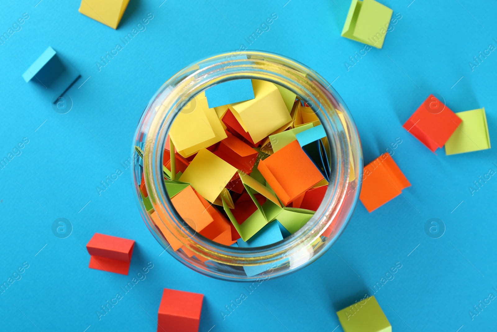 Colorful paper pieces in glass jar on light blue background, top view Photo of Colorful paper pieces in glass jar on light blue background, top view
