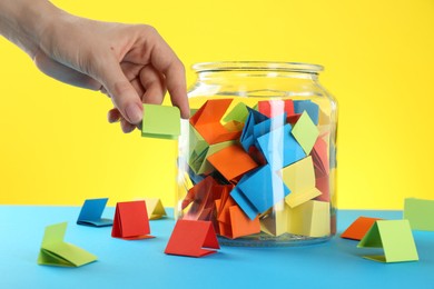 Photo of Woman taking green paper piece from glass jar on color background, closeup