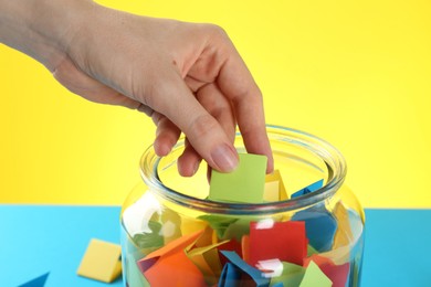 Photo of Woman taking green paper piece from glass jar on color background, closeup