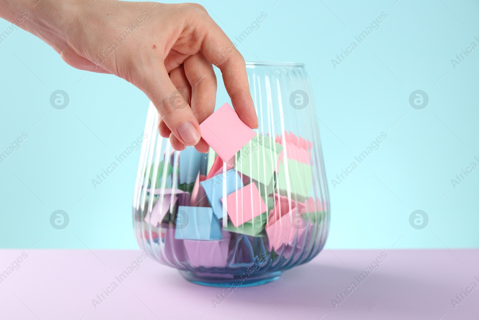 Woman taking pink paper piece from glass jar on color background, closeup Photo of Woman taking pink paper piece from glass jar on color background, closeup