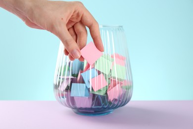 Photo of Woman taking pink paper piece from glass jar on color background, closeup