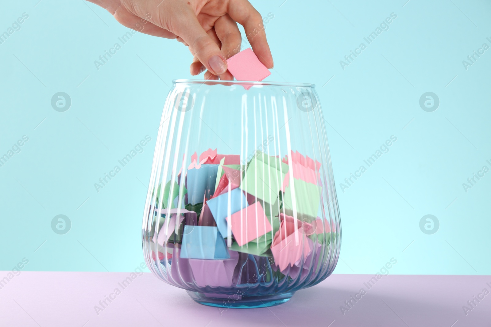 Woman taking pink paper piece from glass jar on color background, closeup Photo of Woman taking pink paper piece from glass jar on color background, closeup