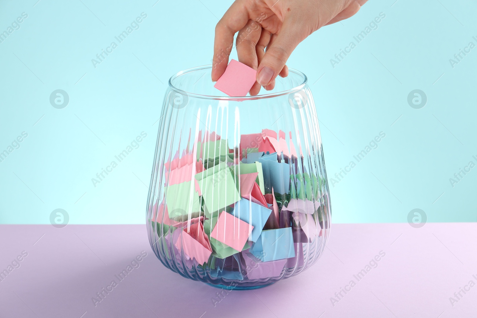 Woman taking pink paper piece from glass jar on color background, closeup Photo of Woman taking pink paper piece from glass jar on color background, closeup
