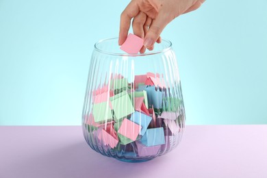 Photo of Woman taking pink paper piece from glass jar on color background, closeup