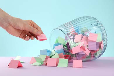 Photo of Woman taking pink paper piece from glass jar on color background, closeup