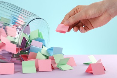 Photo of Woman taking pink paper piece from glass jar on color background, closeup