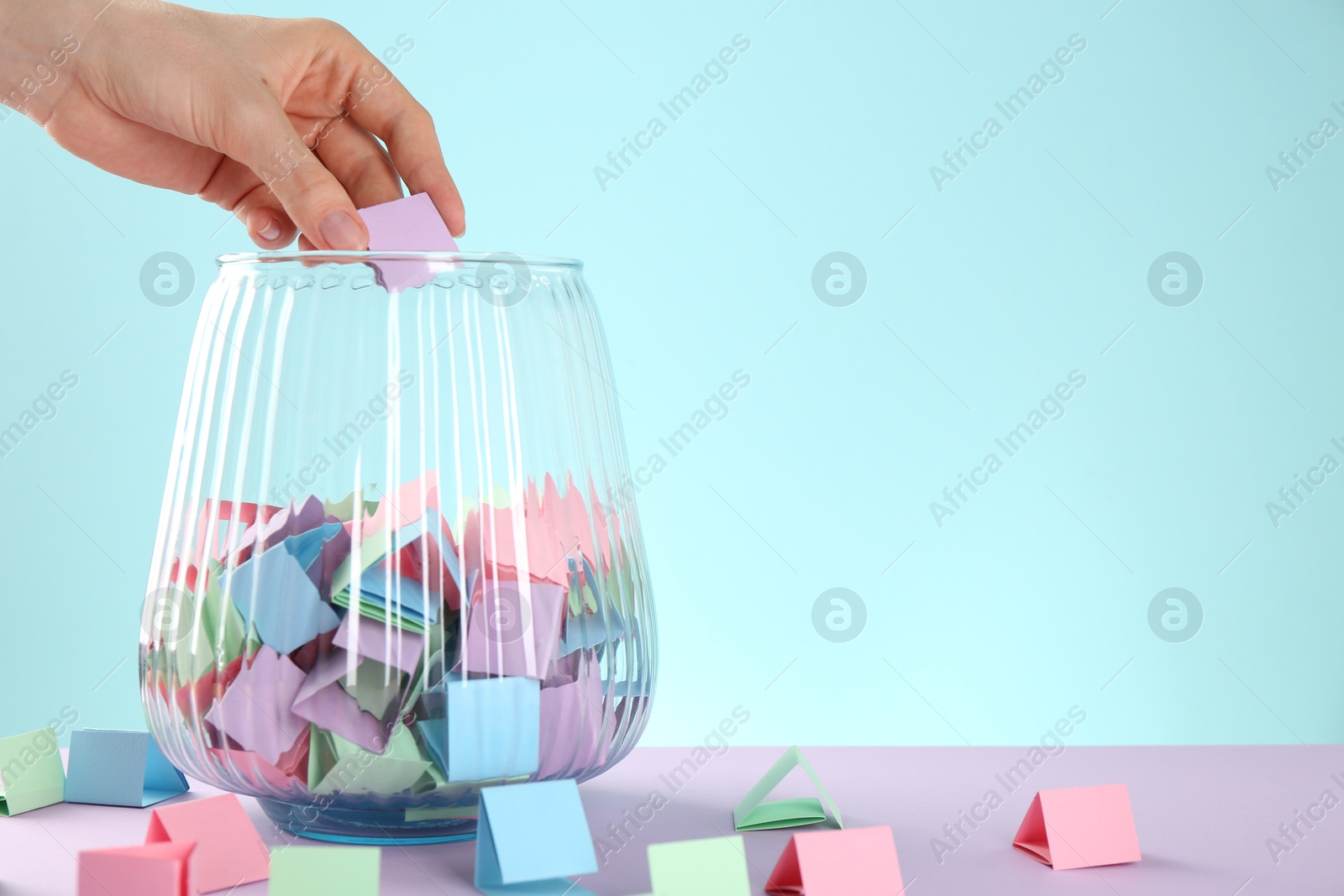 Woman taking violet paper piece from glass jar on color background, closeup. Space for text Photo of Woman taking violet paper piece from glass jar on color background, closeup. Space for text